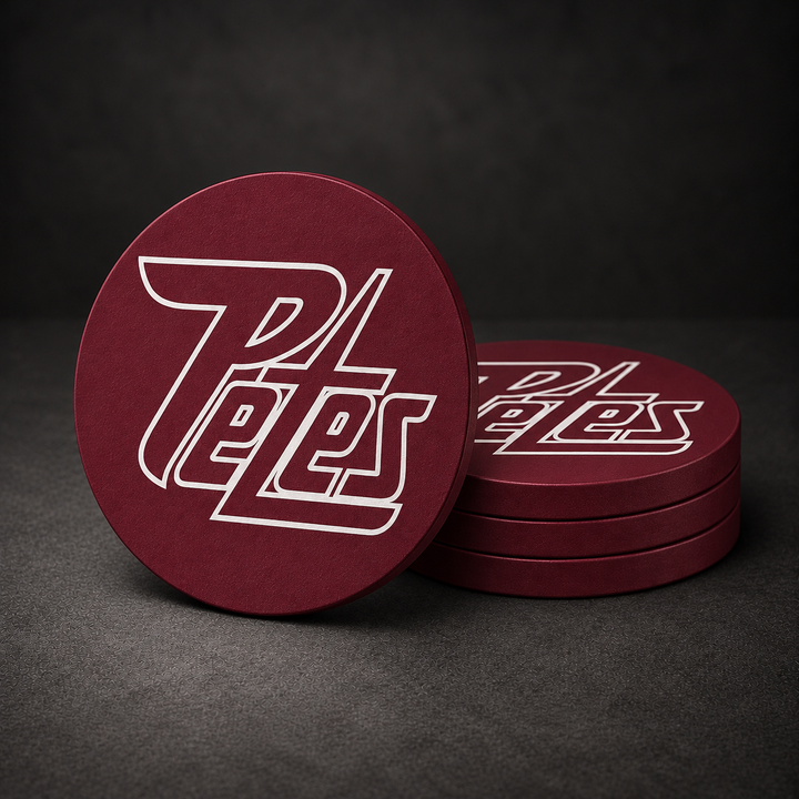 Peterborough Petes Drink Coasters with burgundy red sides, three stacked and one standing on a dark charcoal background